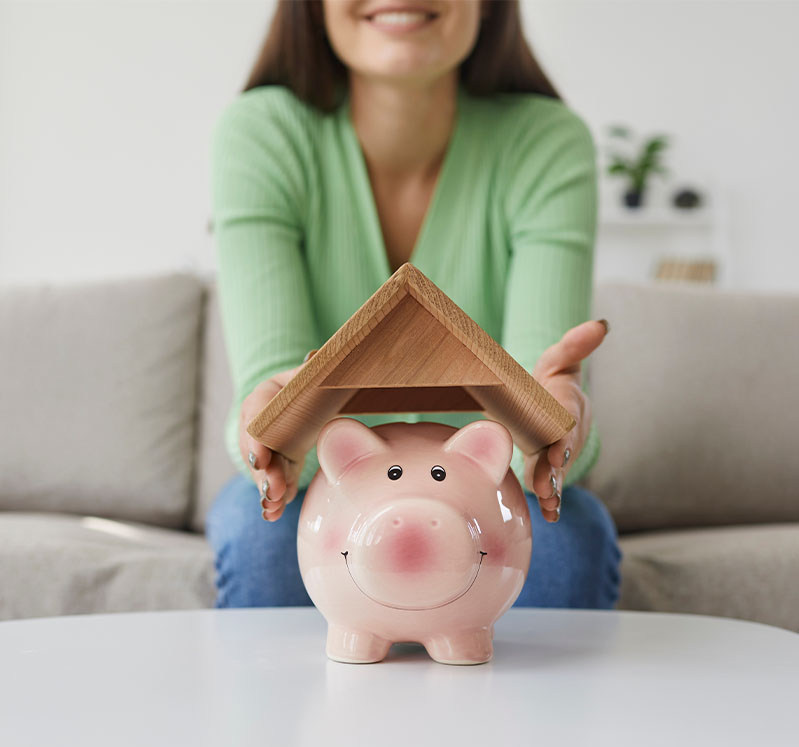 Image showing a close up of a woman holding a model roof over a piggy bank