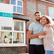 Image showing a happy couple in front of a house with a "Sold" sign