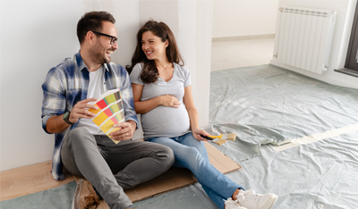 A young, beautiful, and cheerful couple, consisting of a man and his pregnant wife are seated on the floor of an empty house. They are in the process of selecting colors for decorating their new home