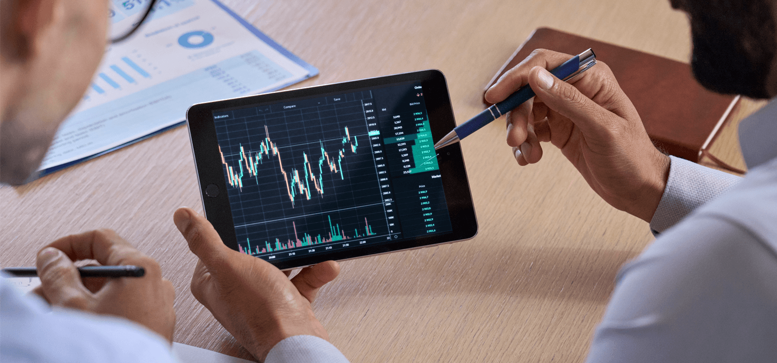 Trader consulting business investor showing crypto trading chart using digital tablet. Over shoulder view